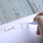 Woman writing thank you on card or paper. Close up view.